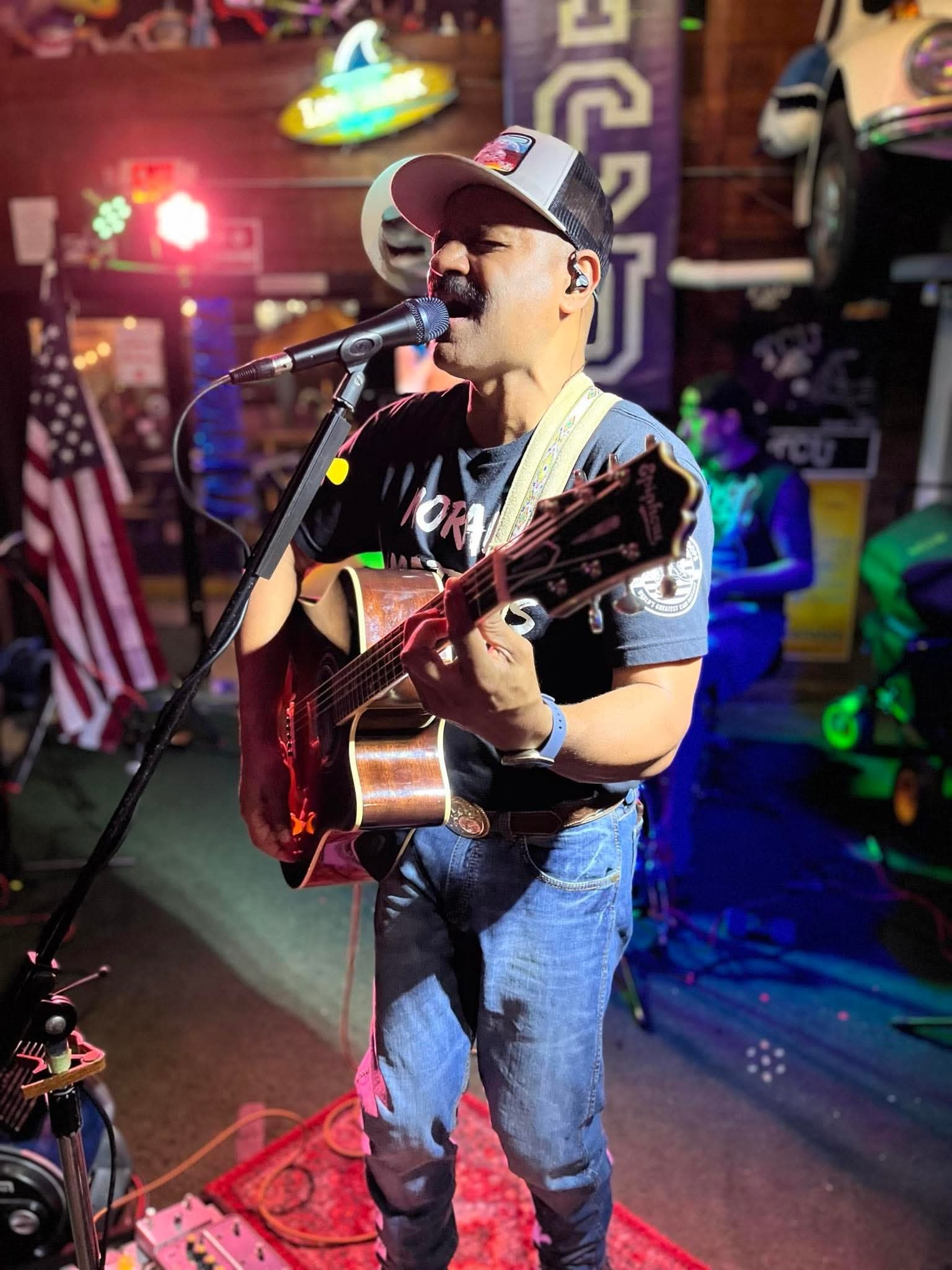 Nigel singing in a trucker cap with acoustic guitar