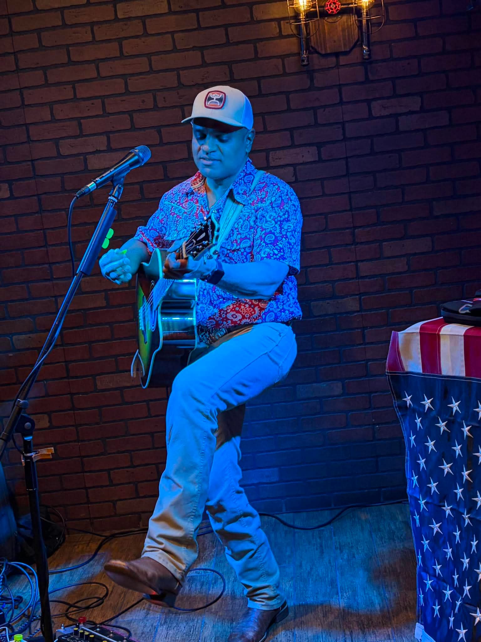 Nigel playing guitar in front of a brick wall in blue light