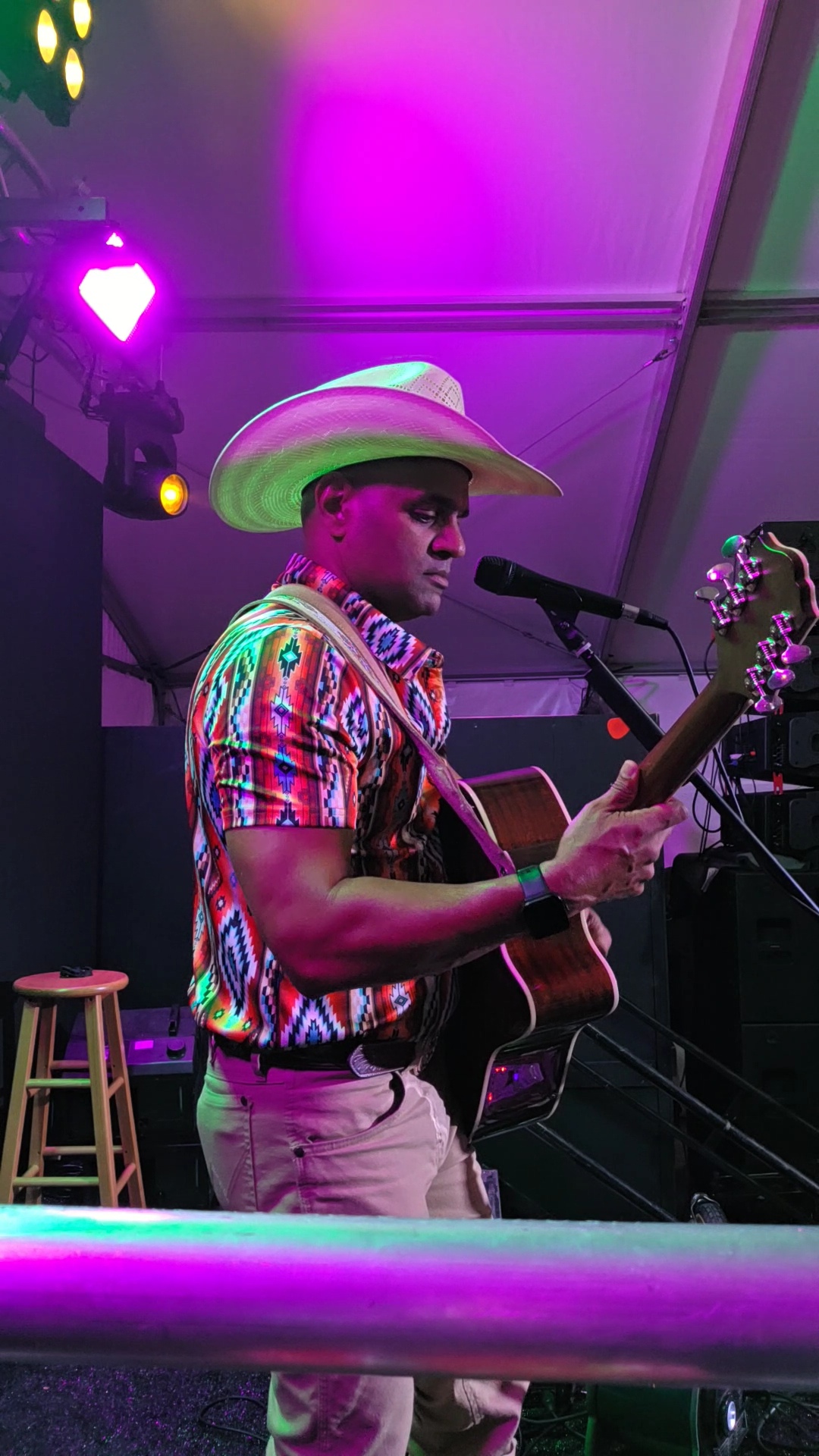 Nigel Edison playing acoustic guitar on stage in a straw cowboy hat under purple lights